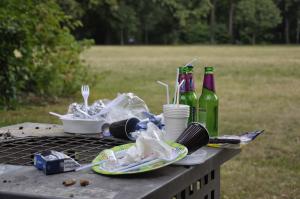 auf einem Mülleimer in einem Park türmt sich benutztes Plastikgeschirr und leere Glasflaschen