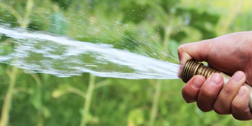 Wasser spritzt aus einem Gartenschlauch, den eine Hand hält