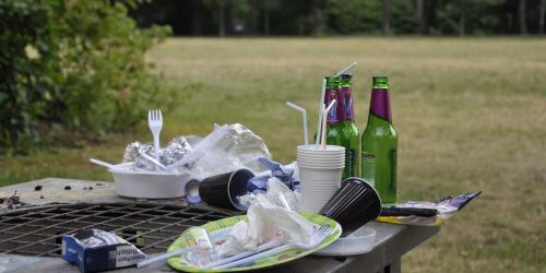 auf einem Mülleimer in einem Park türmt sich benutztes Plastikgeschirr und leere Glasflaschen