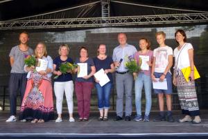 Neun Menschen auf einer Bühne, teilweise mit Urkunden und Blumensträußen