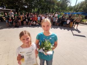im Vordergrund: zwei Mädchen mit Urkunde und Blumen, im Hintergrund Kinder der Leonardoschule