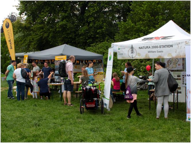 Weißer Pavillon Natura2000-Stationen im Vordergrund und grauer Pavillon Ethikbank hinten, Besucher im Gespräch