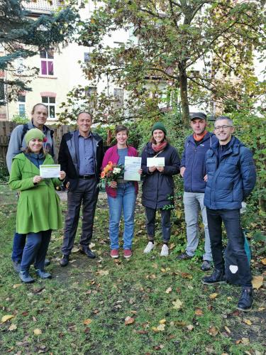 Preisübergabe im grünen Hinterhof, Preisträgerin mit Blumenstrauß und Urkunde